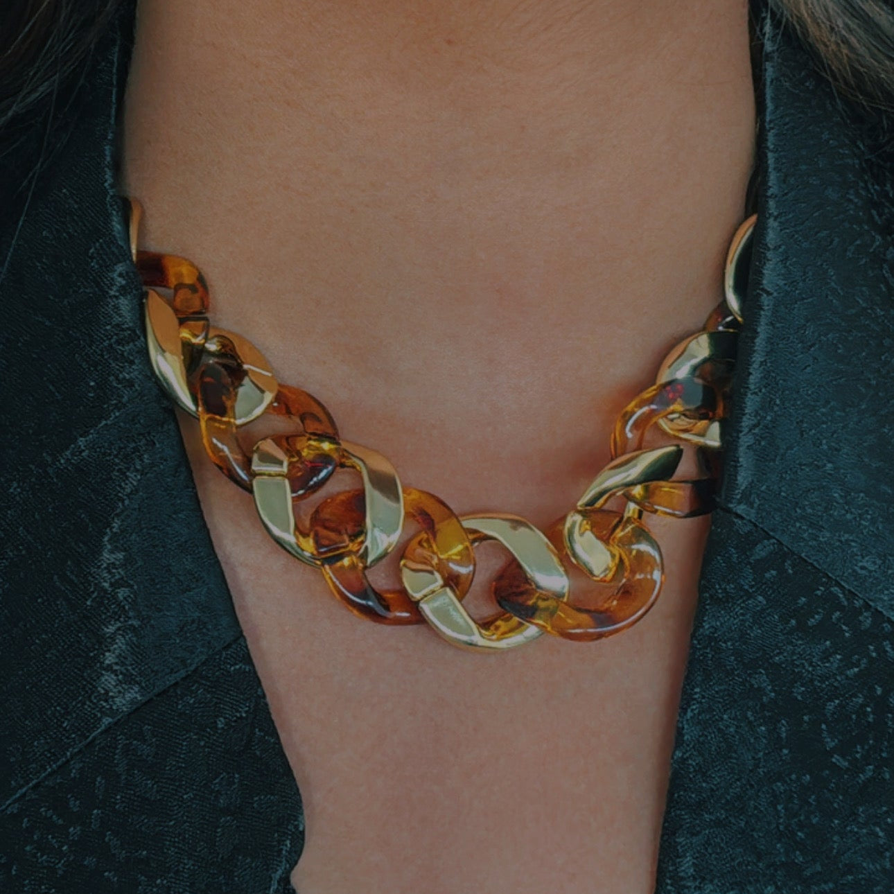 Close-up of a person wearing a gold and amber chain necklace.